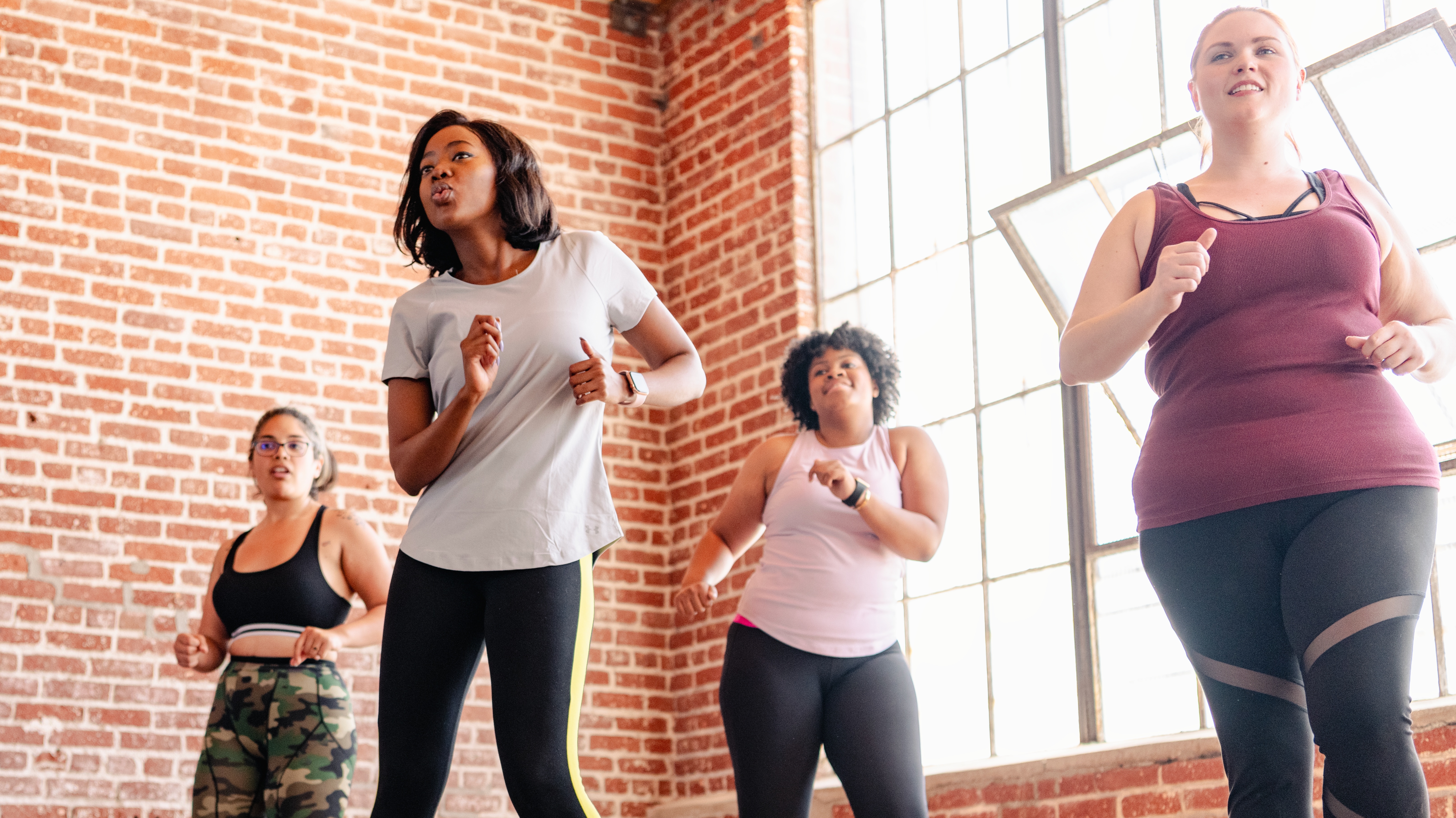 women in workout clothes exercising in room with brick walls and industrial windows