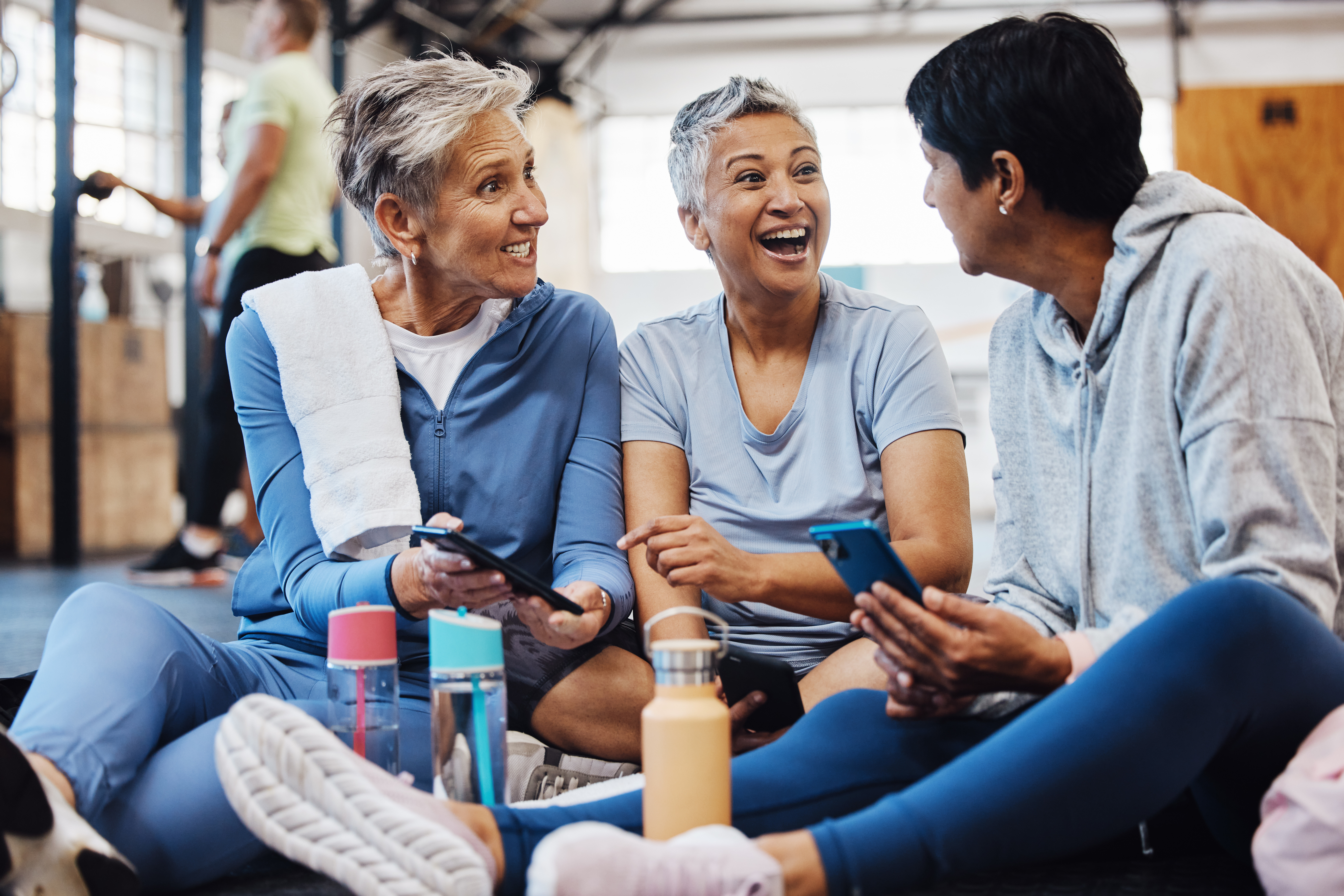 three women sitting on the floor in workout clothes happily talking